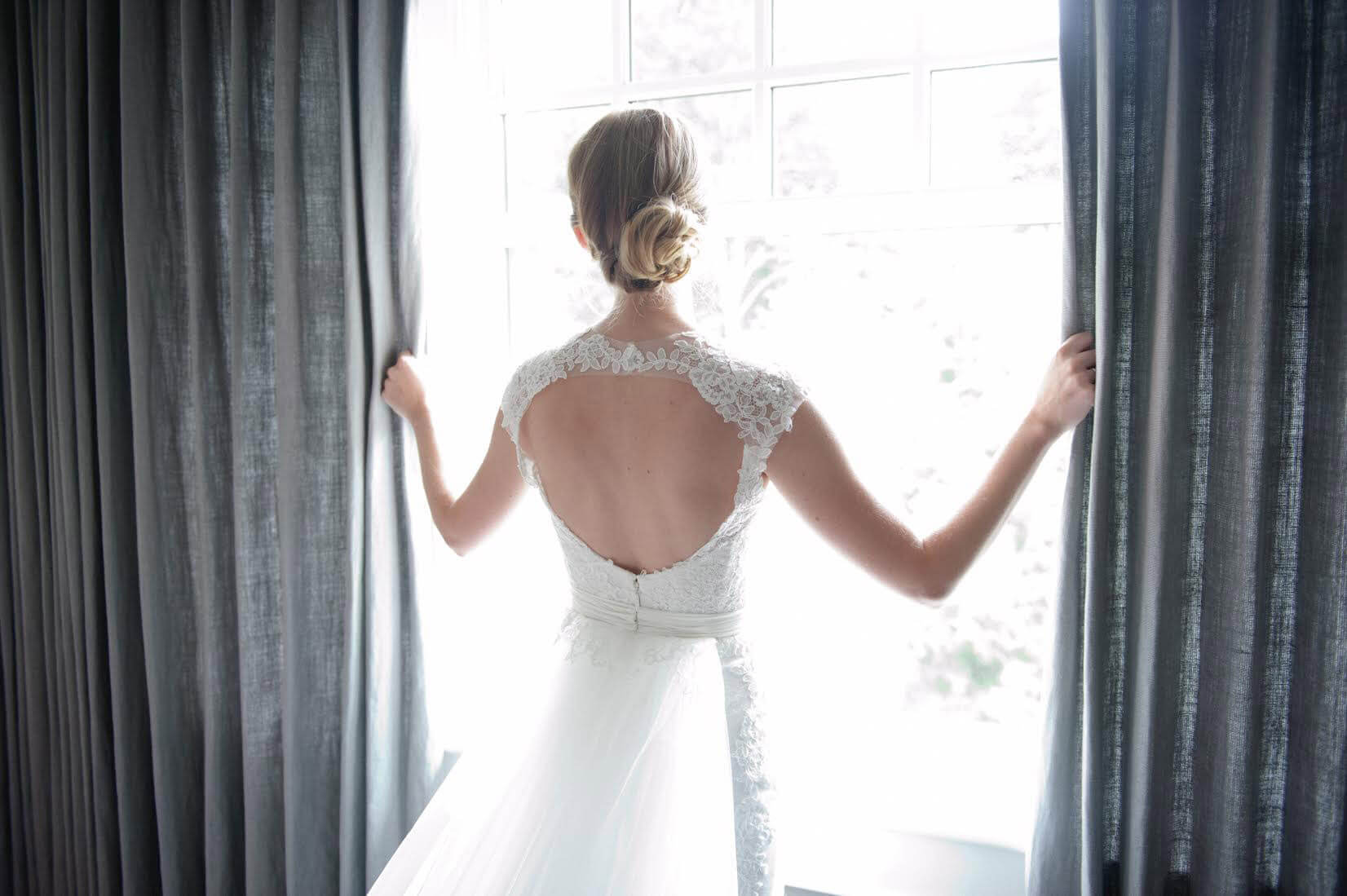A bride in her dress gazes out the bay window of her parents Ottawa home before her wedding. Photo by AMBphoto